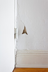 Damaged property: white wall behind a door hinge with a crack or rip and a piece of plaster missing. Refurbishment of real estate concept.