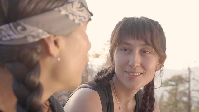 Two Native American hikers having a conversation while seated in golden hour. The woman is in focus.