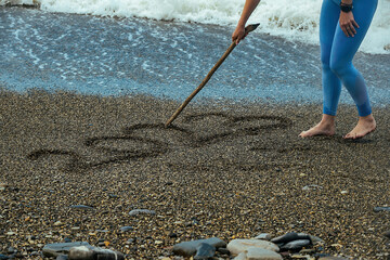 tourist girl writes numbers of the new year 2023 on the seashore with a stick