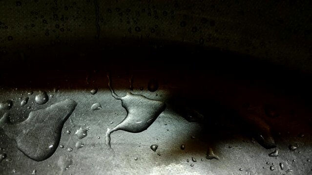 Close-up of water drops slowly flowing down a metal surface.