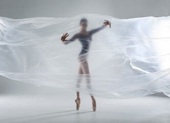 Ballerina in dark ballet leotard dancing on ballet pointe shoes in white studio 