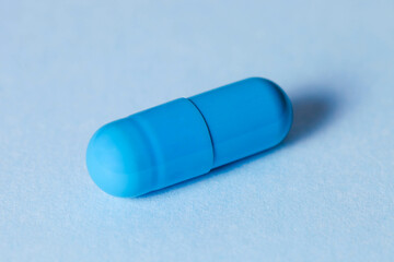 One blue medicine capsule on blue background. Dietary supplement.