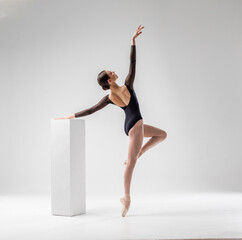 Ballerina in dark ballet leotard dancing on ballet pointe shoes in white studio  - obrazy, fototapety, plakaty
