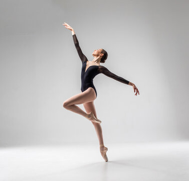 Fototapeta Ballerina in dark ballet leotard dancing on ballet pointe shoes in white studio 