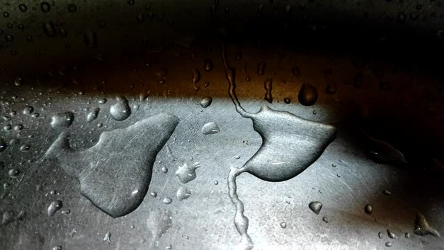 Close-up of water drops slowly flowing down a metal surface.