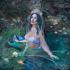 A fantastic woman, a beautiful mermaid girl is sitting on the rocks, with a beautiful hairstyle and...