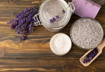 Obraz na płótnie Canvas Lavender spa. Sea salt, lavender flowers, essential oils, body cream and handmade soap. Natural herbal cosmetics with lavender flowers on brown texture background. Relax and spa concept.Space for text