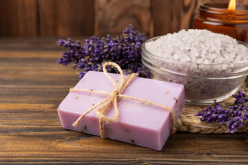 Obraz na płótnie Canvas Lavender spa. Sea salt, lavender flowers, essential oils, body cream and handmade soap. Natural herbal cosmetics with lavender flowers on brown texture background. Relax and spa concept.Space for text