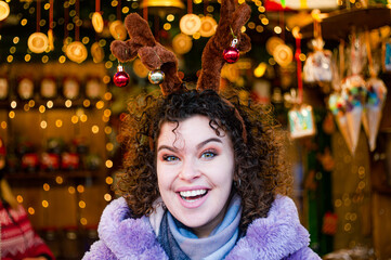 Smiling curly haired woman in trendy violet coat drinks mulled wine outdoors 