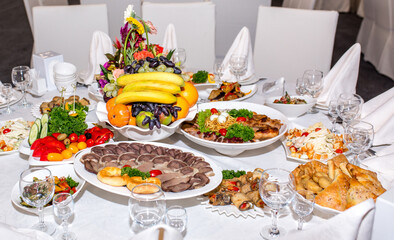 Table setting in a restaurant. Table decorated with flowers and beautiful appetizers salads on a white tablecloth. Holiday dinner.