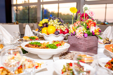 Table setting in a restaurant. Table decorated with flowers and beautiful appetizers salads on a white tablecloth. Holiday dinner.