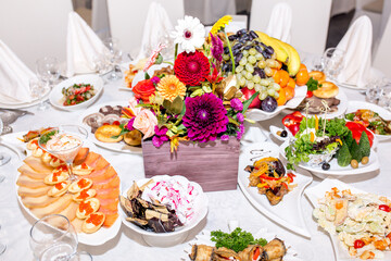 Table setting in a restaurant. Table decorated with flowers and beautiful appetizers salads on a white tablecloth. Holiday dinner.
