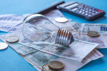 ncandescent lamp, Russian money and a calculator on a blue background. The concept of energy saving, payment for electricity