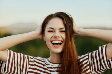A young woman in a striped T-shirt sincerely laughs with her mouth open while traveling against the...