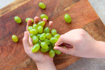 a woman's hand with green grapes, wooden background, concept of fresh sweet fruits and healthy food