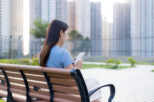 Woman Use Mobile Phone And Sit On Bench