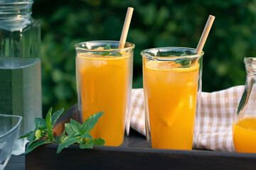 Refreshing summer homemade orange cocktail in tall double glass glasses with mint and ice, selective focus