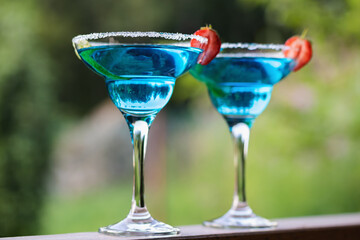 Two glasses with blue margarita cocktail garnished with lime zest and strawberries, selective focus