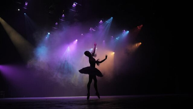 Graceful hard-working ballerina dancing i in spotlight. Silhouette   Diligent ballet dancer performing dancing elements of classical ballet. Slow motion.