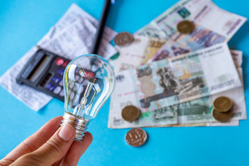An incandescent lamp in a hand against the background of Russian money and electricity bills. The...