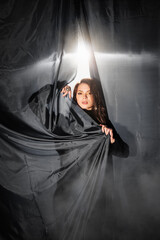 Languid young woman in elegant long dress leans against black curtain in studio