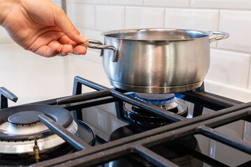 Female hand holding saucepan standing on the gas burner of the stove.
