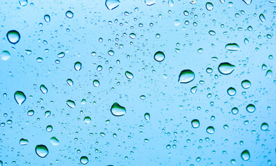 Rain outside the window. Water droplets on a car glass on a background of blue sky and green grass. Overcast. Wet clean nature, ecology
