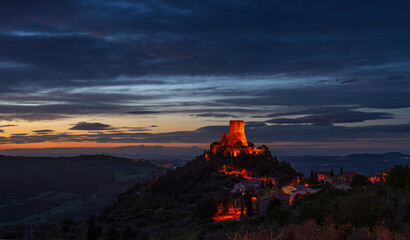 Rocca d'Orcia, a medieval village and fortress in Tuscany, Italy. Unique view at dusk, the stone tower perched on rock cliff against dramatic sky.