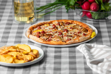 Bavarian pizza (mozzarella cheese, alpine sausages, baked potato wedges, bacon, sweet peppers, barbecue sauce) on a white plate on the table.