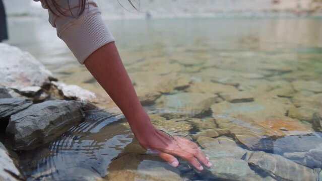 Female hand touching water in the calm Himalayan Lake during summer time. At Deepak Tal, Himachal Pradesh. Traveler enjoying feel the nature. Life concept. Slow motion shot.