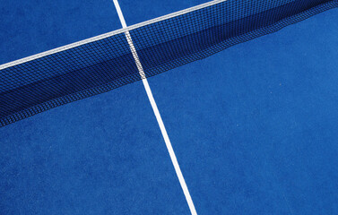 View of the net and the centre line of a blue paddle tennis court.