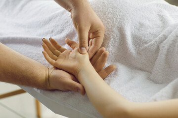 Professional reflexologist doing remedial hand massage to female patient. Reflexology and acupressure therapy specialist pressing and affecting special points and areas on young girl's palm. Close up