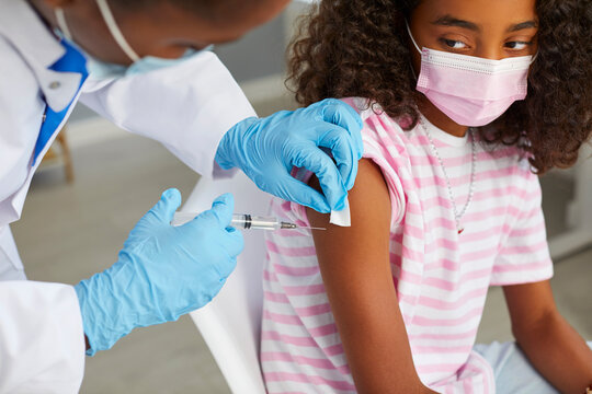 Protection And Immunization Of Population With Covid-19 Vaccine. Nurse Gives Covid 19 Vaccine To Dark-skinned Teenage Girl Who Is Sitting In Medical Mask. Doctor Disinfects Injection Site. Close Up.