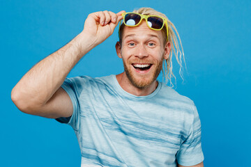 Naklejka premium Full body smiling young blond man with dreadlocks 20s he wear white t-shirt sunglasses point index finger aside isolated on plain pastel light blue background studio portrait. People lifestyle concept