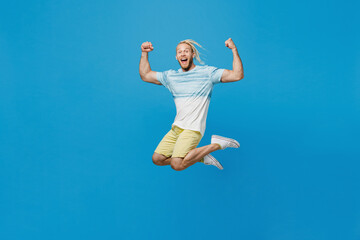 Full body young blond man with dreadlocks 20s he wear white t-shirt look camera jump high do winner gesture isolated on plain pastel light blue background studio portrait. People lifestyle concept.