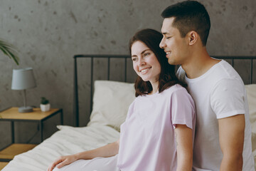 Fototapeta premium Side view young fun happy lovely two woman man she he wear casual t-shirt pajama cuddle hug sitting in bed rest spend time together in bedroom lounge home in own room hotel. Real estate family concept