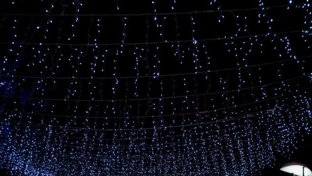 Tracking shot of bright icicle led string lights outdoor on black celebration sky, shiny Christmas street illumination.