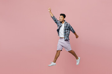 Fototapeta na wymiar Full body side view young defender man of African American ethnicity wear blue shirtjump high do super hero gesture clench fist isolated on plain pastel light pink background People lifestyle concept