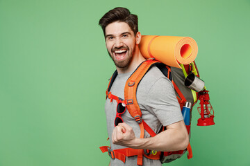 Side view young traveler white man carry backpack stuff mat show thumb up isolated on plain green...