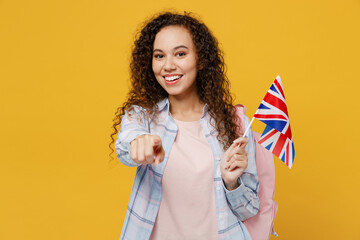 Young happy black teen girl student she wear casual clothes backpack bag hold british flag point finger camera on you isolated on plain yellow color background. High school university college concept.