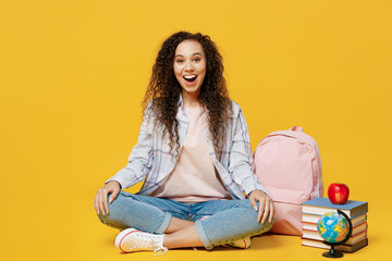 Full body exultant happy young black teen girl student she in casual clothes backpack bag sitting on floor near books isolated on plain yellow color background High school university college concept