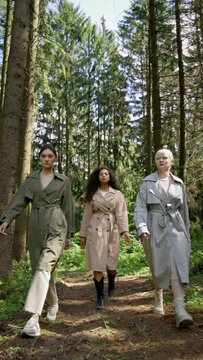 Three models with different skin colors walk along a forest path, vertical video
