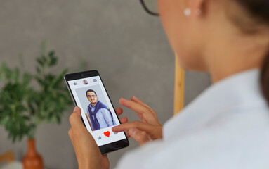 Single woman uses smartphone to find love. Woman using dating app on mobile phone and swiping user photos and pressing red button. Close up of smartphone with open profile of man. Selective focus.