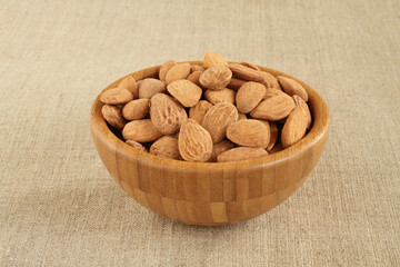 Big shelled roasted salted almonds in bamboo bowl on rough linen cloth . Closeup. Day light