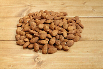 A heap of raw almonds on brown toned wooden table.