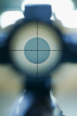 View through the scope of a sniper rifle at a target with bullet holes in the top ten.