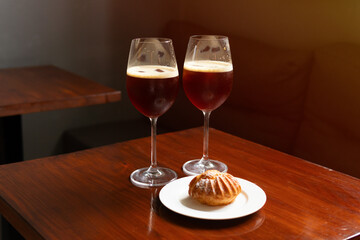 Nitro cold brew coffee drink with ice in coffee shop cafe, alternative coffee, v60. Two glasses with a soft drink and a profiterole dessert on the table. High quality shot.