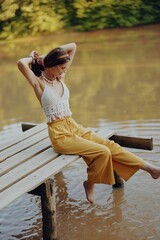 A young happy hippie woman sitting on the lake shore on a bridge in eco clothing made of natural materials in harmony with nature in the fall