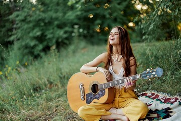 Young female hippie artist plays guitar and sings songs in eco-friendly clothing sitting on the...