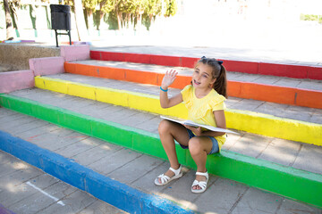 Fototapeta na wymiar Cute girl sitting on a staircase with the colors of the LGTBI flag, picking up a notebook. 